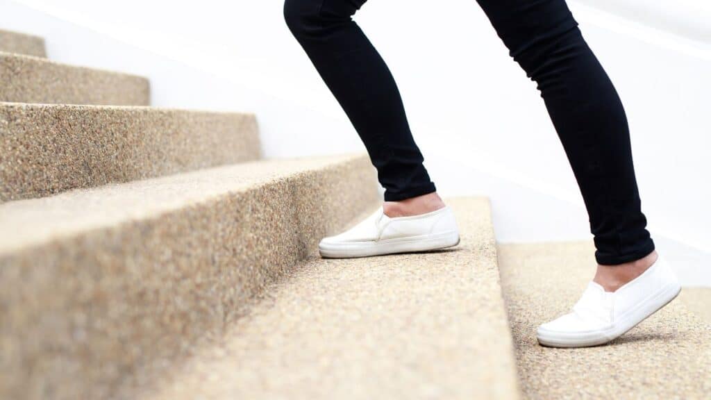Person walking up outdoor steps wearing white sneakers and black leggings, staying active to hit 10000 steps a day.