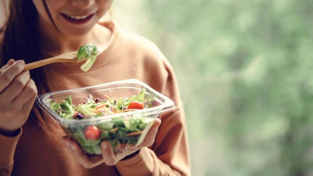 Close-up of a woman eating a fresh salad with leafy greens and cherry tomatoes, reflecting the nutritional benefits of seasonal foods for a healthy lifestyle.