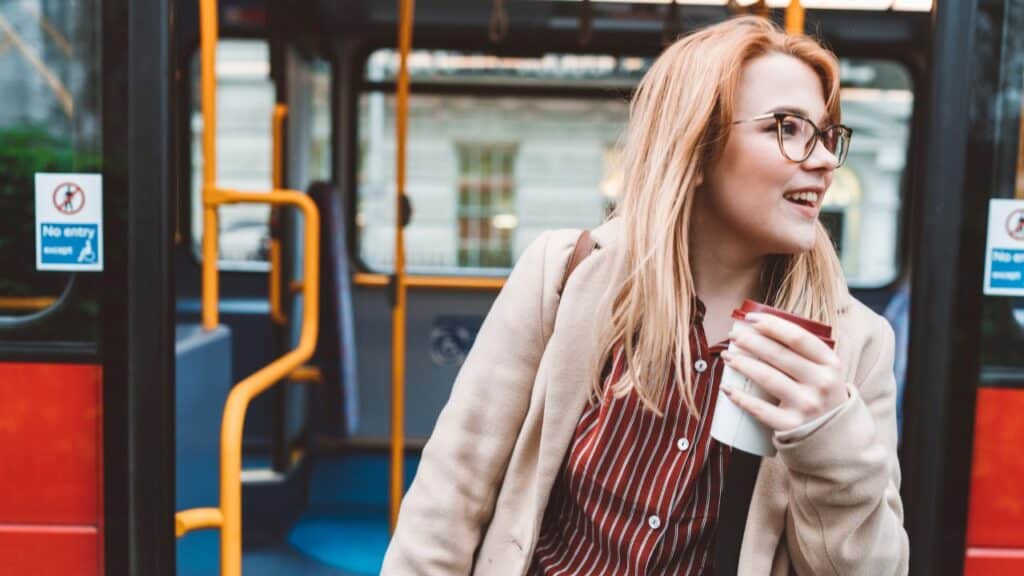Woman stepping off a city bus holding a coffee cup, incorporating movement into her commute to hit 10000 steps a day.