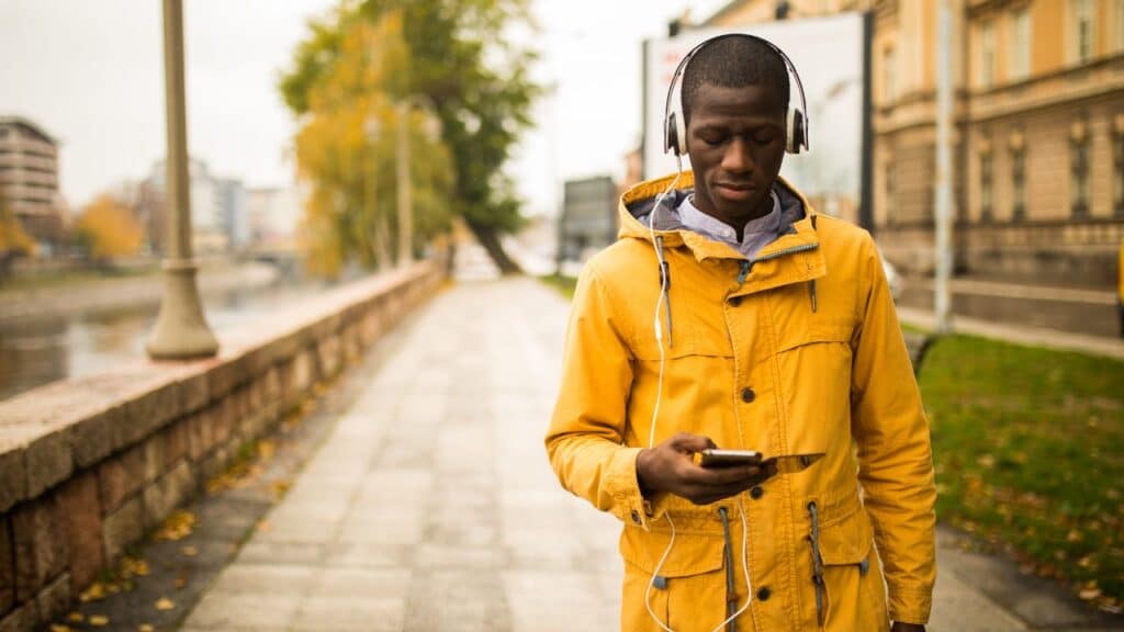 Man walking outdoors in a yellow jacket while listening to music on headphones, enjoying a stroll to hit 10000 steps a day.