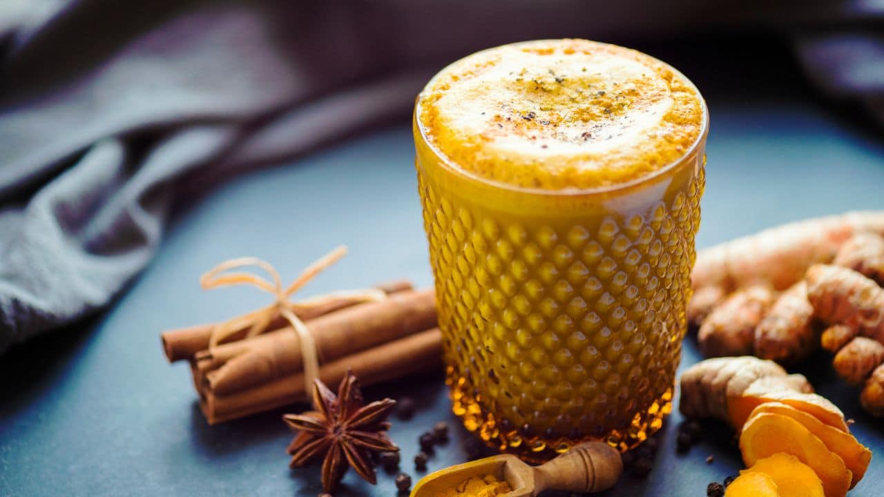 A golden turmeric latte served in an ornate glass, surrounded by cinnamon sticks, star anise, and turmeric roots. A warming beverage for nutritious breakfast tips with added health benefits.