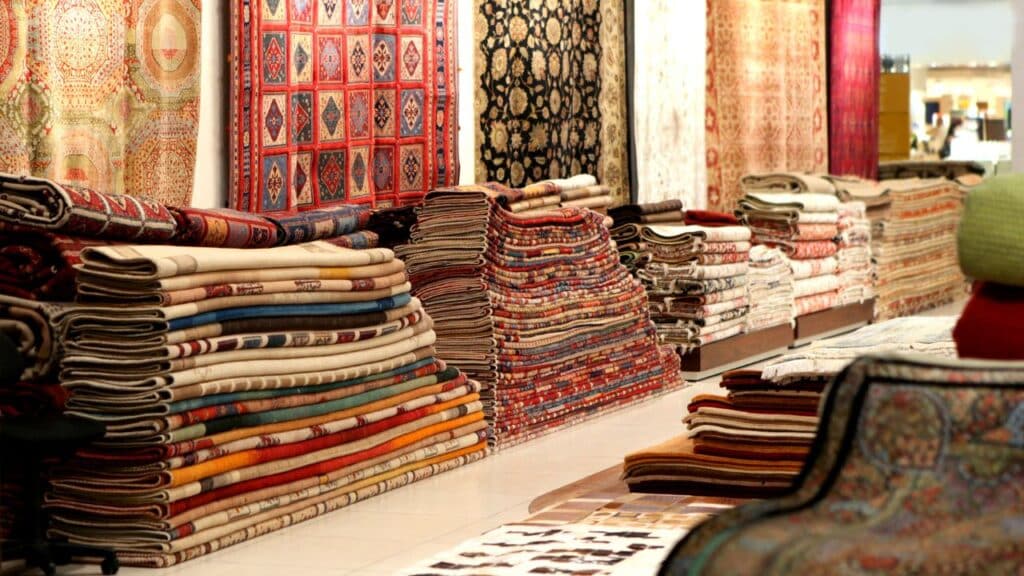 A variety of colorful patterned rugs stacked in a store, offering texture and style to elevate your home decor.