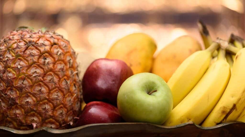 Close-up of a fruit basket with pineapple, apples, bananas, and mangoes, celebrating the nutritional benefits of seasonal foods for energy and wellness.