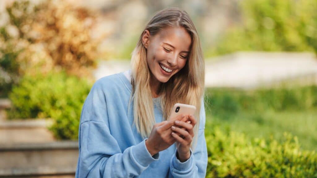 Smiling woman sitting outside looking at her phone, taking a break during a walk.