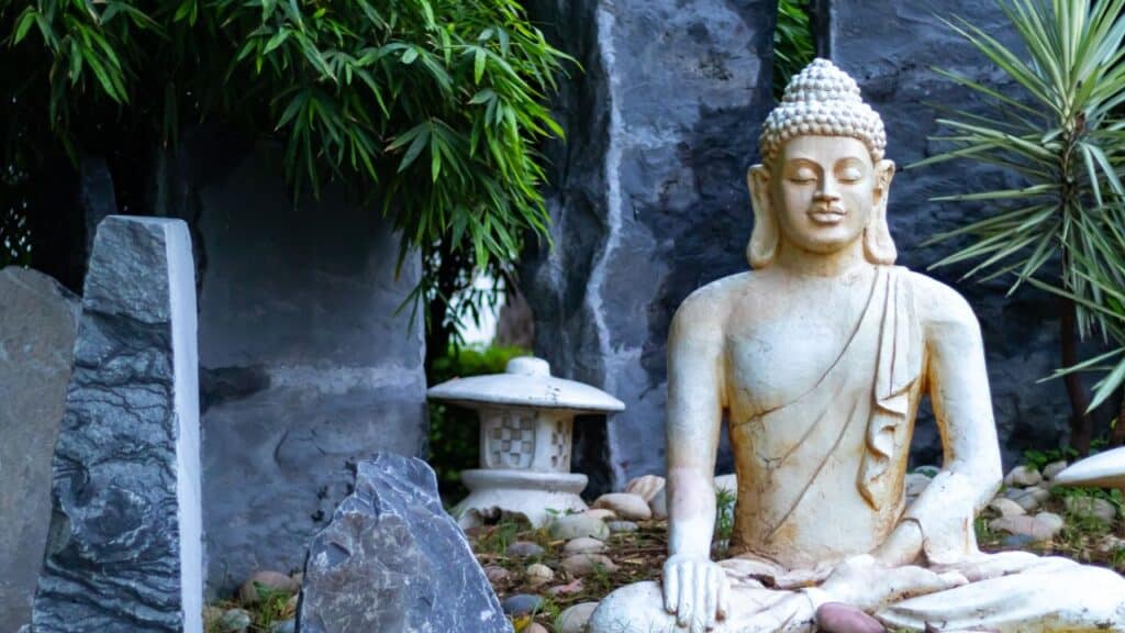 A serene garden corner featuring a stone Buddha statue surrounded by rocks and greenery, adding a calming Zen element to outdoor spaces.