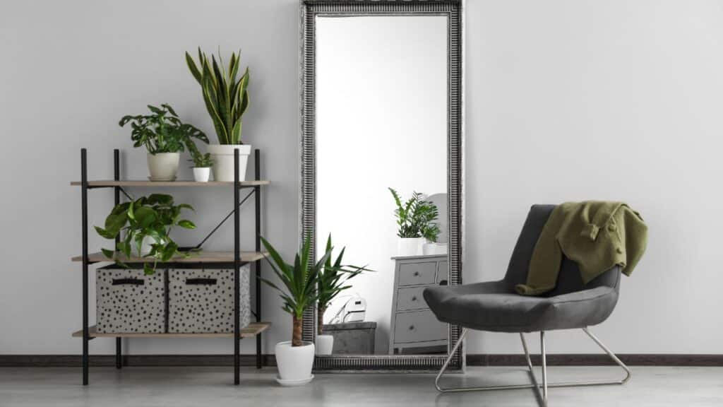 A large standing mirror with a metal frame, paired with houseplants and a cozy chair, brings depth and freshness to elevate your home decor."