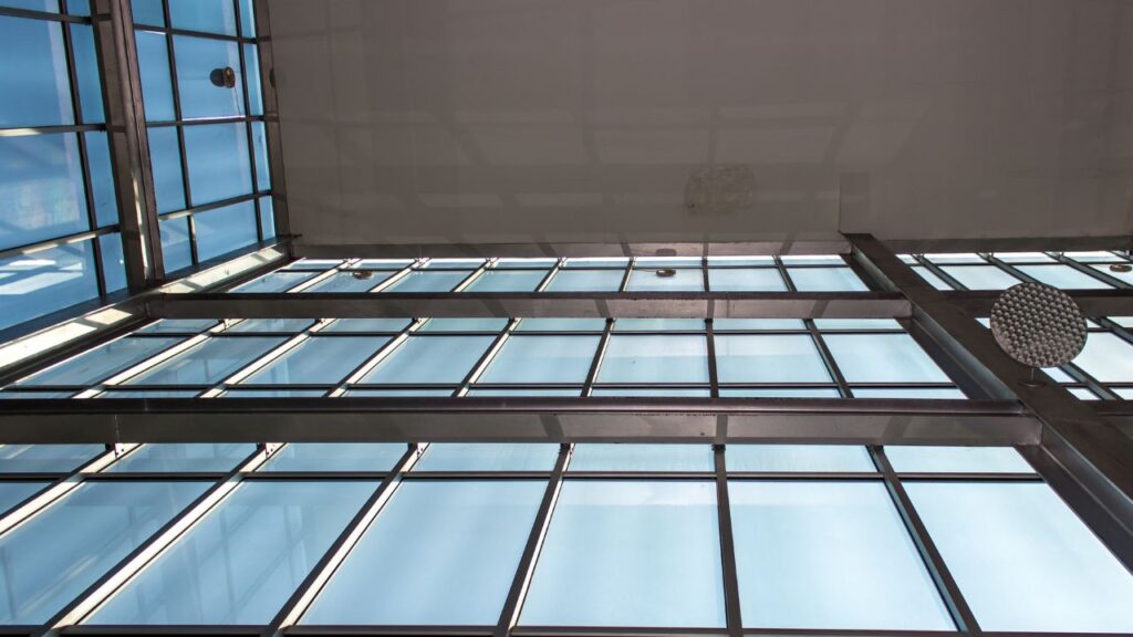 A view of a large ceiling skylight with steel framing and frosted blue glass emphasizes the open, light-filled architecture often seen in 70s' home design trends.