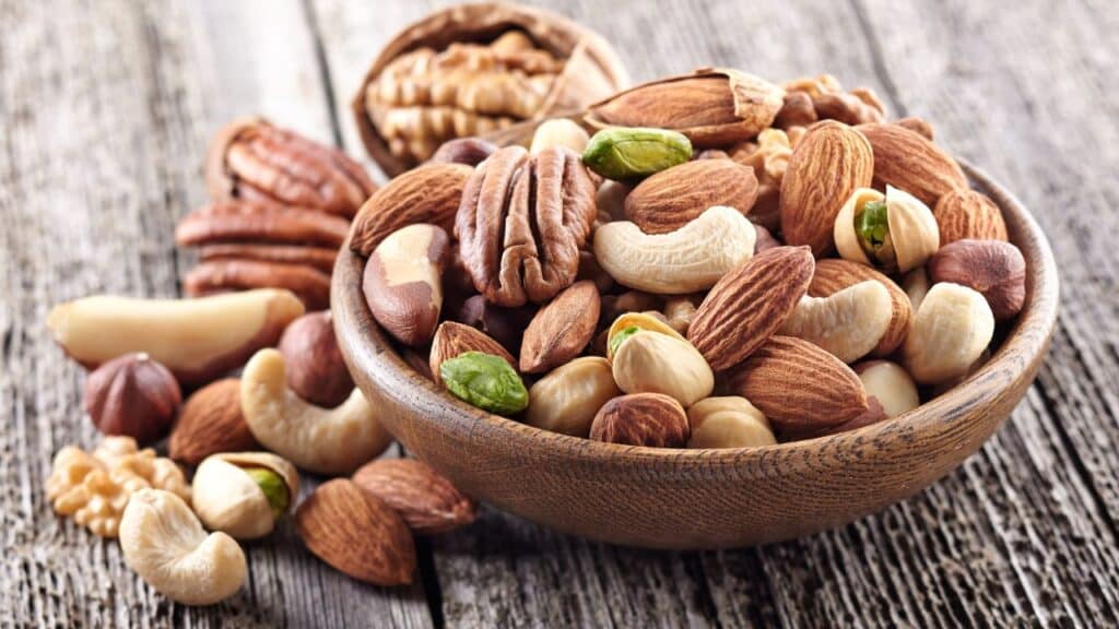 A wooden bowl filled with assorted nuts including almonds, cashews, and walnuts on a rustic table. Nuts are nutrient-dense and are key anti-aging foods.