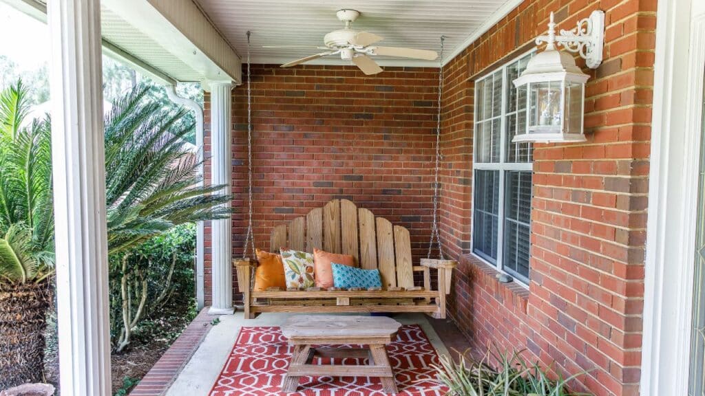 A charming front porch swing with colorful cushions and a patterned rug, creating a welcoming outdoor retreat.