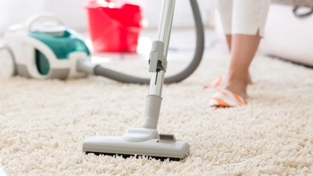 Person vacuuming a carpet with a canister vacuum, counting household chores toward hitting 10000 steps a day.