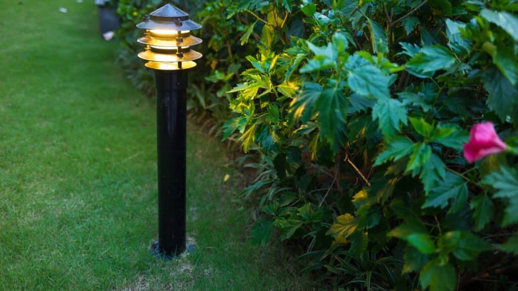 A modern black garden light softly illuminating green foliage, enhancing the cozy ambiance of an evening backyard.