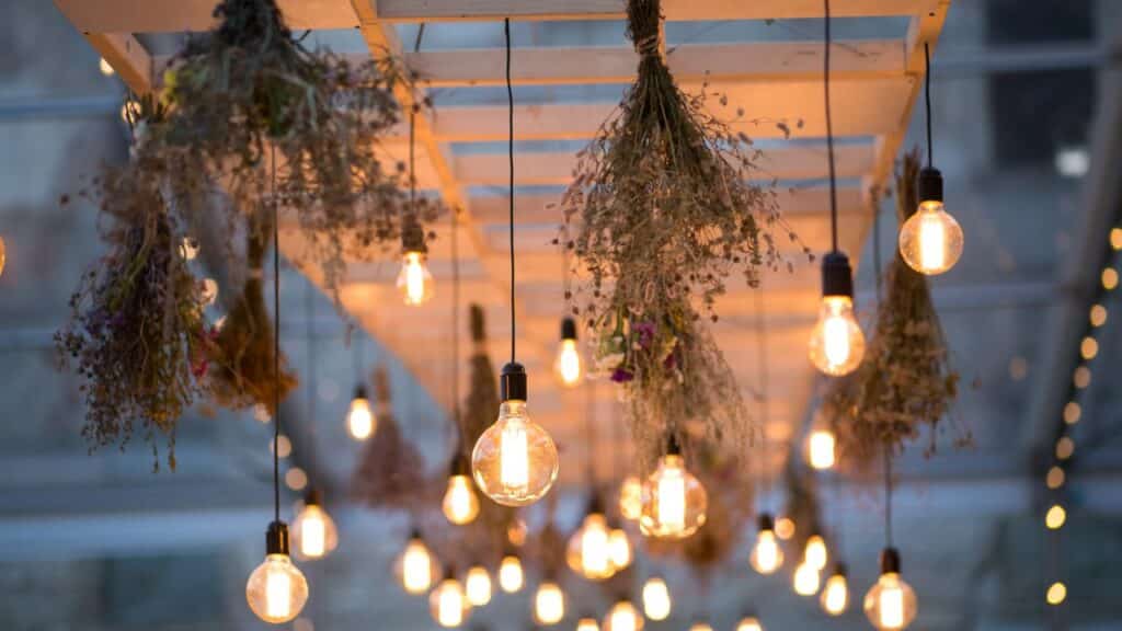 Hanging light bulbs paired with dried floral arrangements on a wooden trellis, adding a warm and inviting touch to backyard decor. A perfect way to turn your backyard into a relaxing haven.