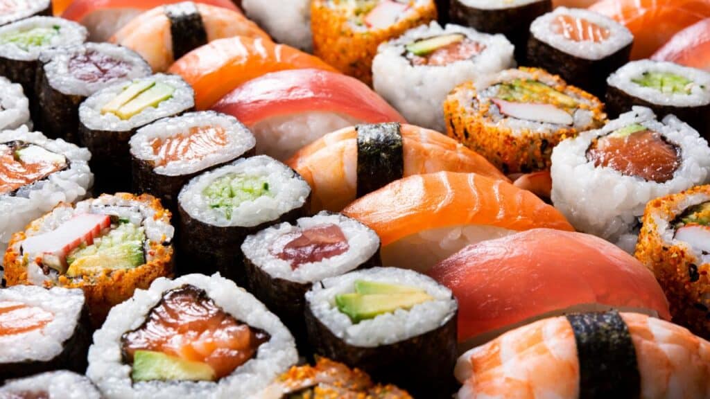 A colorful assortment of sushi rolls and nigiri, featuring salmon, tuna, avocado, and seaweed-wrapped rice pieces. Sushi became a trendy 80s food fad for upscale dining.