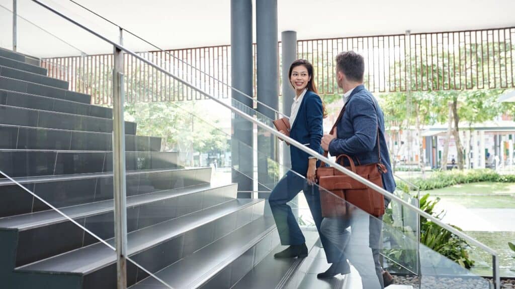 Two professionals walking up modern office stairs, taking steps during the workday to hit 10000 steps a day.