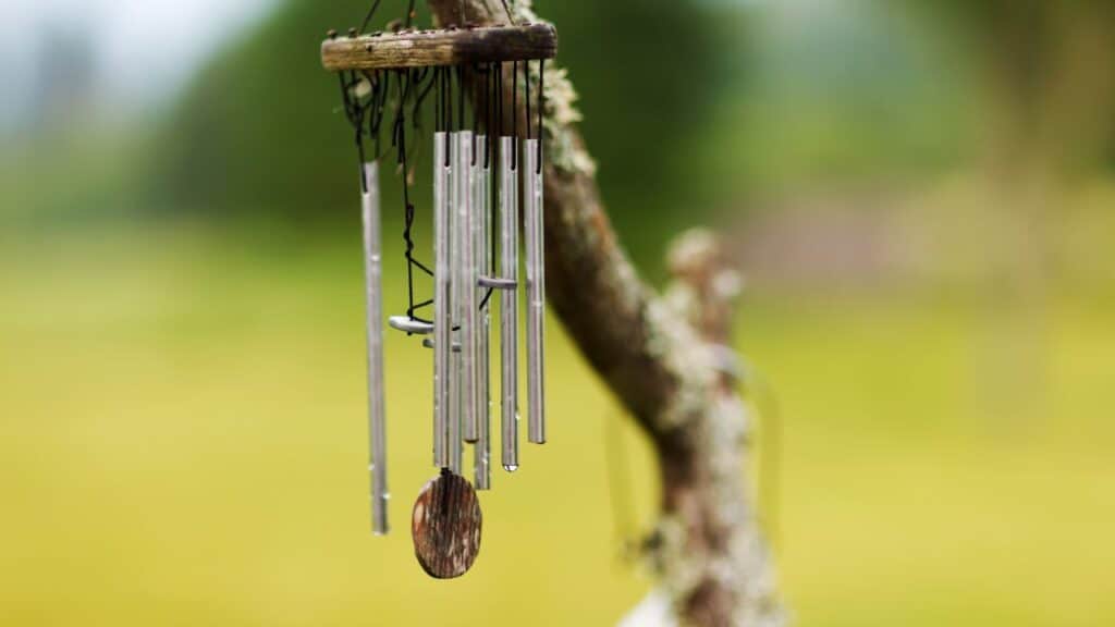 Close-up of silver wind chimes hanging from a tree branch with blurred greenery in the background, adding soothing sounds to an outdoor sanctuary.