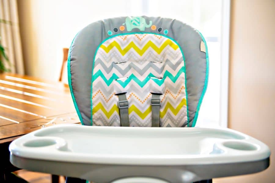 A colorful baby high chair with a chevron-patterned cushion is positioned at a wooden dining table, staged in natural light as if ready for a Facebook Marketplace listing.