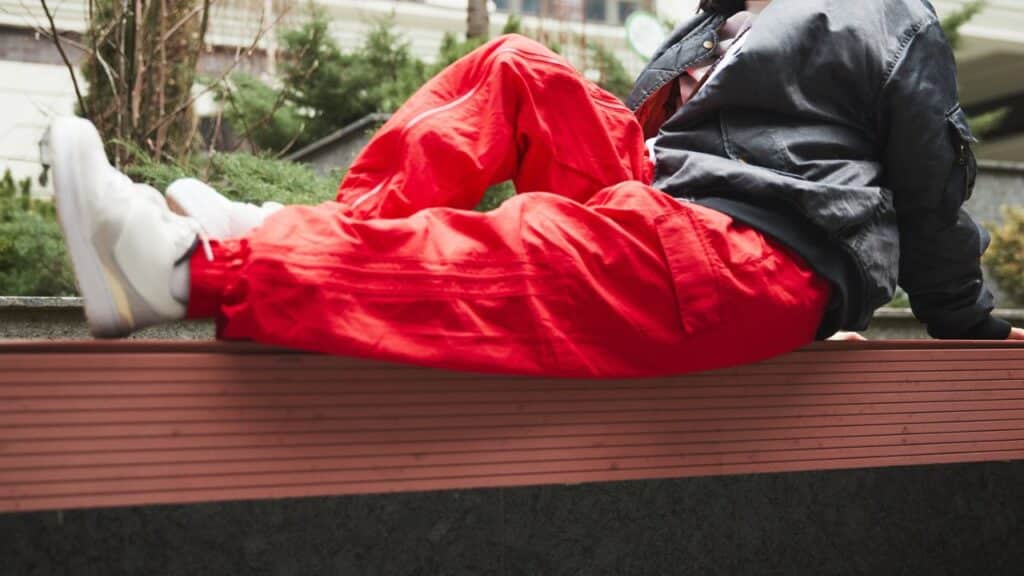Person wearing bright red pants with a black jacket and white sneakers while sitting on a bench, an example of a bold mix that could be a fashion faux pas.