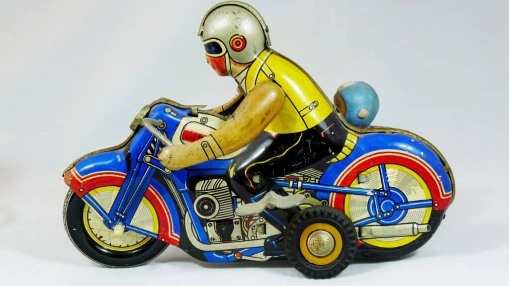 A wind-up tin motorcycle toy with a rider wearing a yellow shirt and silver helmet, painted in bright red, blue, and yellow colors. This mechanical toy was a standout among childhood toys from the 70s.