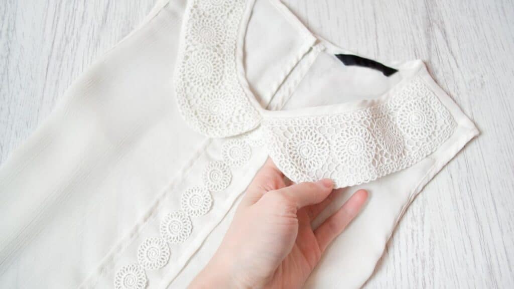 Close-up of a hand holding a white blouse with a large crochet collar, a vintage detail that can easily become a fashion faux pas if styled poorly.