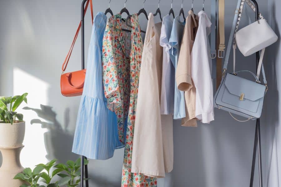 A minimalist clothing rack holds a mix of pastel and floral women’s garments along with handbags, styled as if ready for a Facebook Marketplace fashion post.