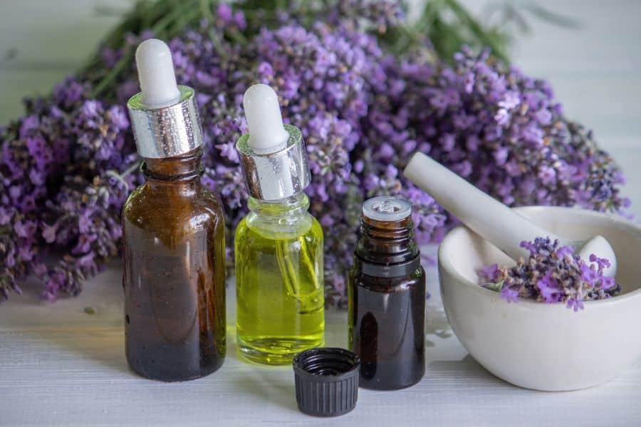 Dropper bottles of essential oils with blooming lavender and a white mortar and pestle in the background. Aromatherapy with lavender oil is one of many soothing nightly rituals that rewind the clock on aging.
