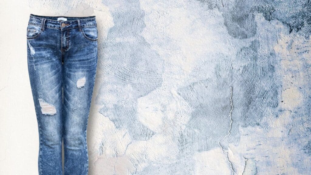 Distressed blue jeans with ripped details against a textured wall, a trendy look that can turn into a fashion faux pas when overdone.