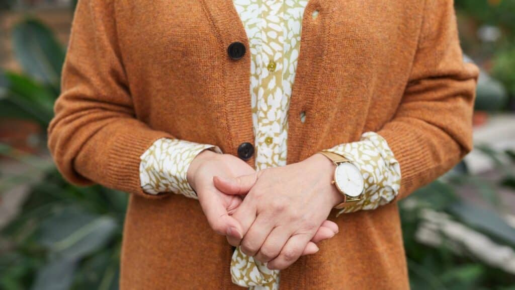 Close-up of a woman wearing an orange cardigan over a patterned blouse with a wristwatch, an outfit combination that may be considered a fashion faux pas.