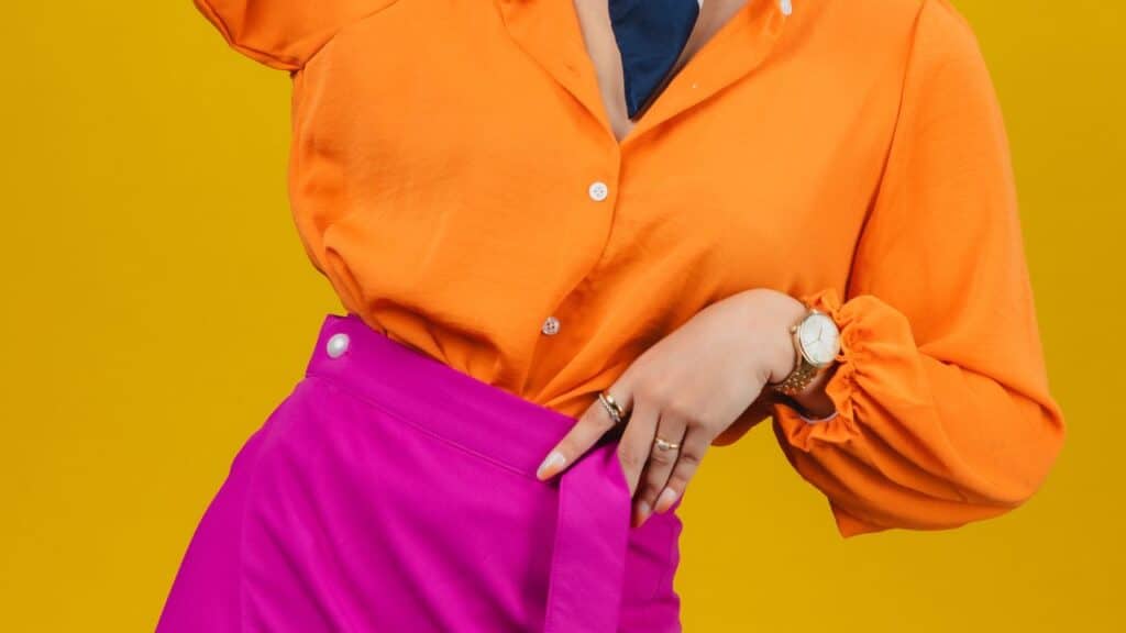 Partial view of a person in an orange blouse tucked into a bright pink skirt, highlighting a clashing color mix often seen as a fashion faux pas.