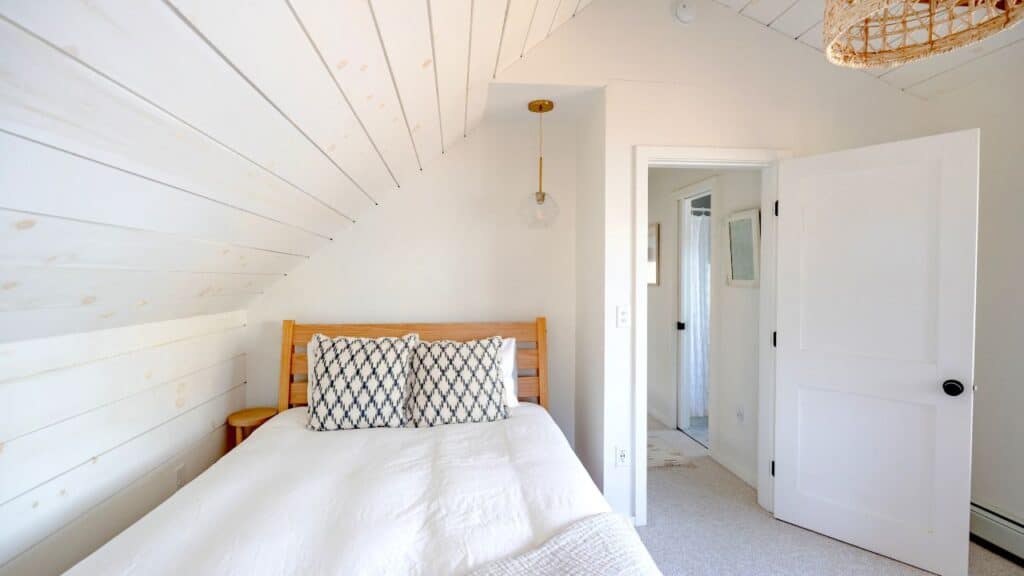 Small attic bedroom with a wooden bed, white bedding, and patterned pillows arranged for balance and harmony following Feng Shui tips.