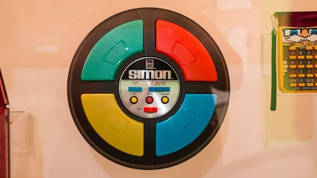The circular Simon electronic memory game with red, green, yellow, and blue light-up buttons is displayed. It became an iconic electronic challenge among childhood toys from the 70s.