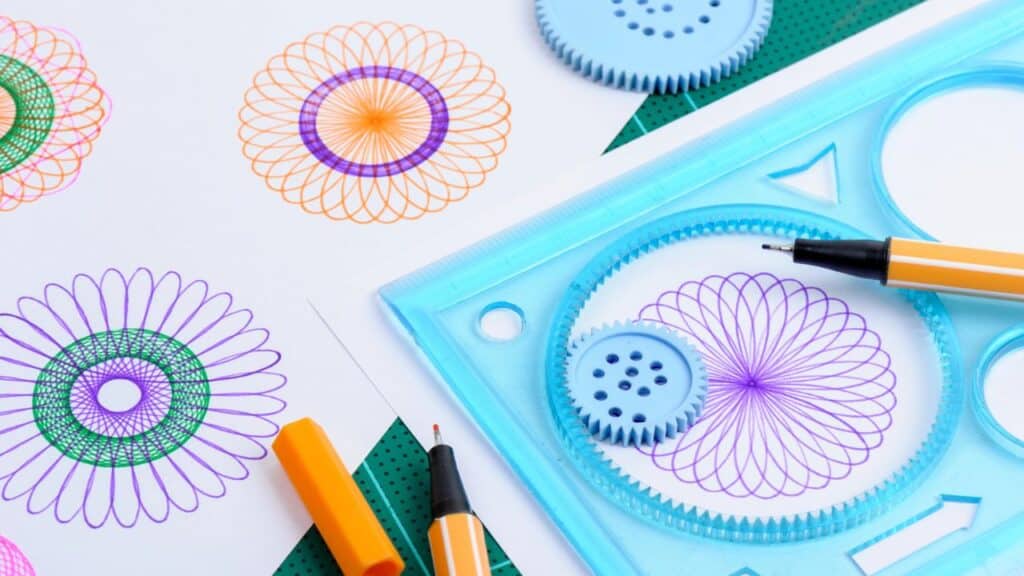 A plastic spirograph kit with gears and pens is shown creating intricate geometric patterns in bright colors. This artistic tool was a creative favorite in childhood toys from the 70s.