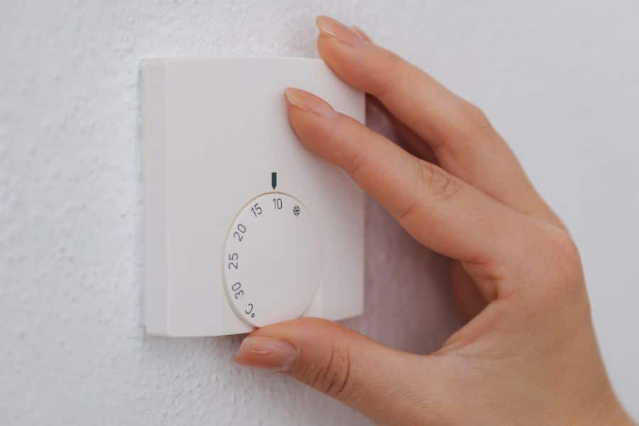 Close-up of a hand adjusting a white dial thermostat set to around 17°C. Maintaining a cool room temperature is a key part of nightly rituals that rewind the clock on aging.