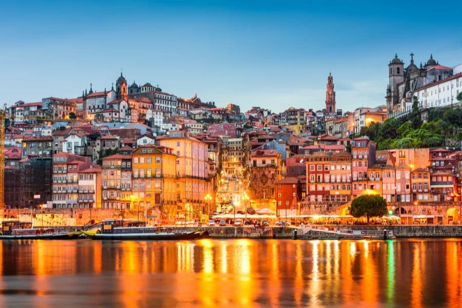 Colorful hillside buildings in Porto, Portugal glow under evening lights, reflecting beautifully across the Douro River. A dreamlike view for Americans dreaming of moving to Europe.
