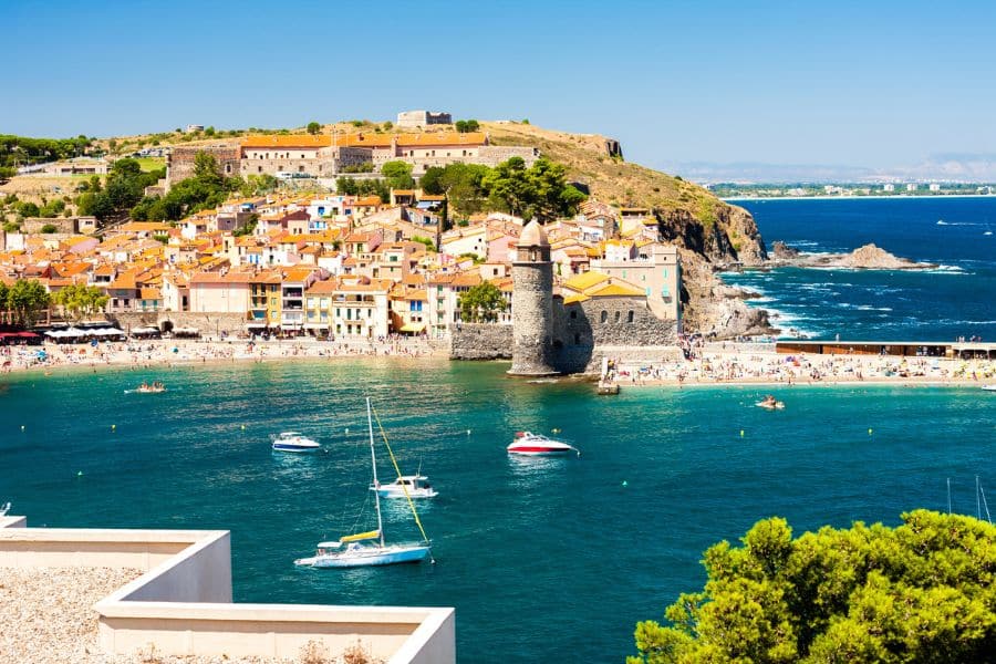 The French village of Collioure with its iconic bell tower, pastel waterfront houses, and boats anchored in the Mediterranean bay. A picturesque coastal village with historic and artistic flair.