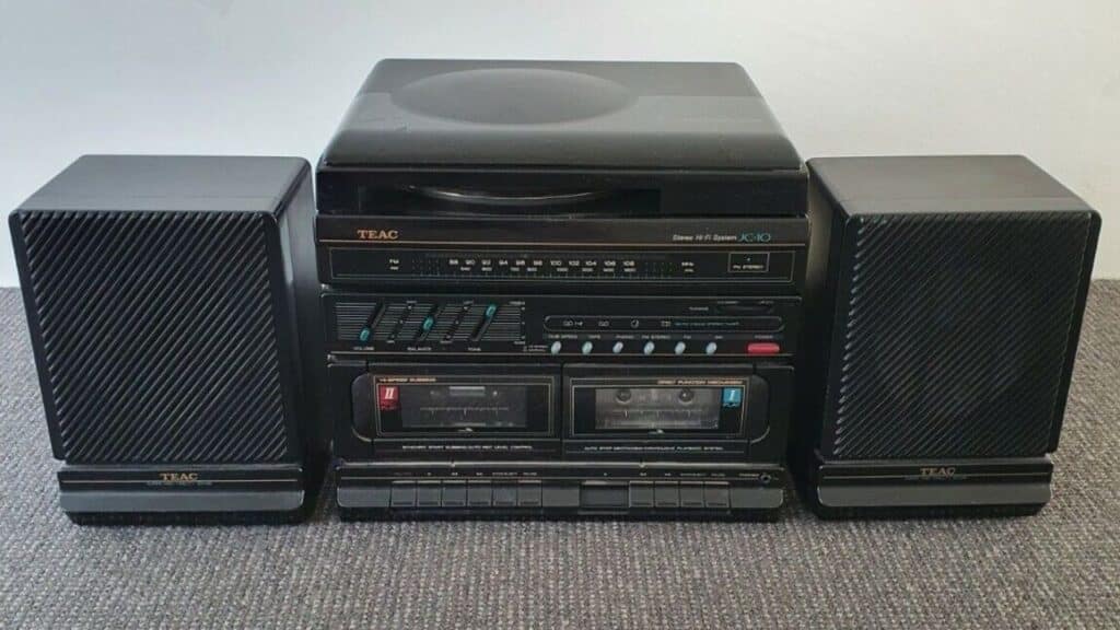 A black TEAC stereo system with dual cassette decks, built-in equalizer, and two large speakers placed on carpeted flooring.
