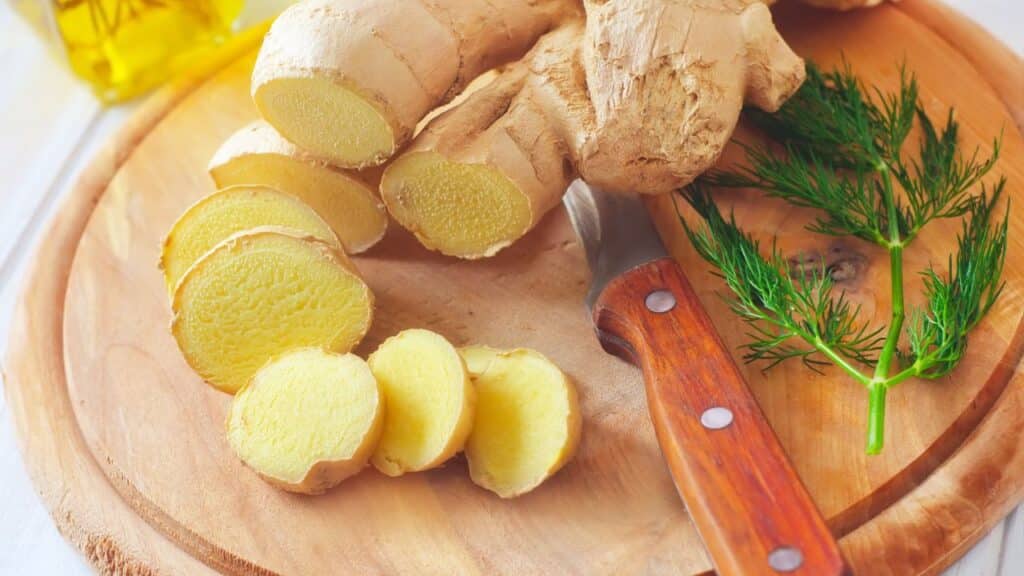 Fresh ginger root sliced on a wooden cutting board with a sprig of dill and a wooden-handled knife. Ginger is a staple in vintage remedies for nausea and inflammation.