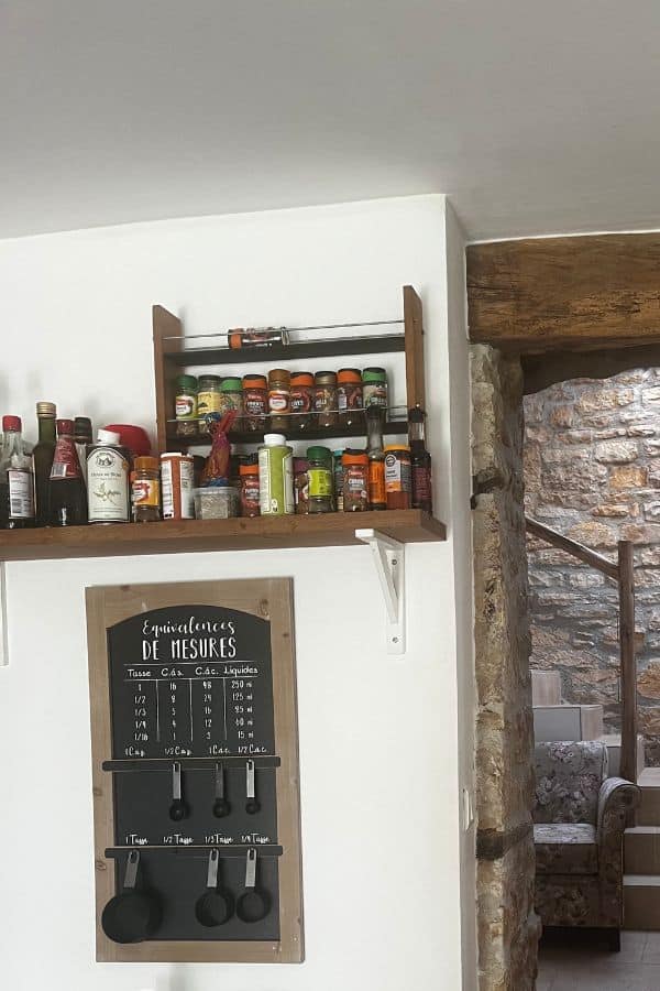 An old kitchen wall with a framed blackboard with measuring cups and spoons on it.