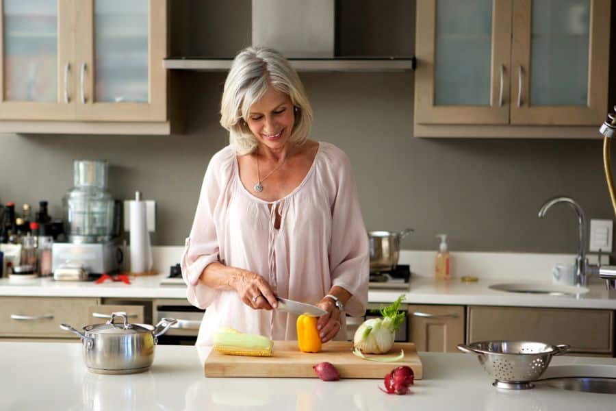A woman slices a bell pepper in a modern kitchen, showing cooking or meal prep services as creative retiree-friendly jobs.
