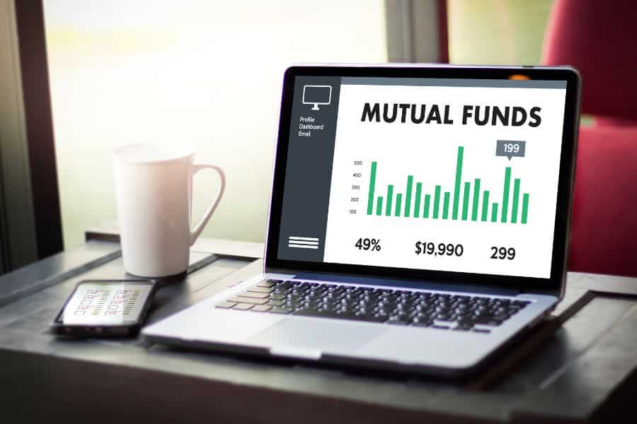 Laptop screen displaying mutual fund performance metrics beside a coffee cup and smartphone. Suggests diversifying real estate strategies through investment vehicles like REITs or mutual funds.