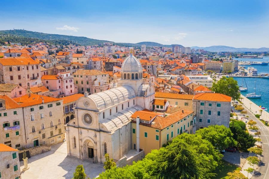 The coastal city of Šibenik, Croatia, featuring the white stone St. James Cathedral surrounded by terracotta-roofed buildings and a scenic harbor. A historic European coastal village blending medieval architecture and seaside elegance.