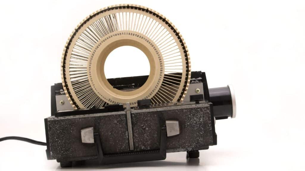 A vintage slide projector with a circular carousel filled with photographic slides, shown against a white background.