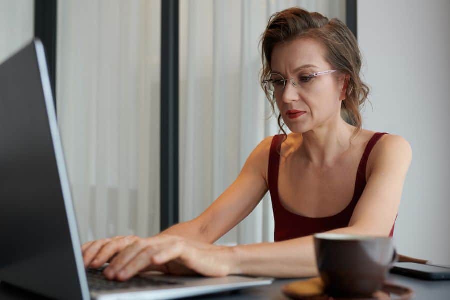 A focused woman types on a laptop with a coffee nearby, representing freelance writing or virtual assistant work as retiree-friendly jobs that offer flexibility.