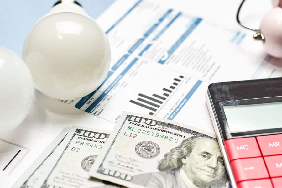 Energy bills, calculator, and lightbulbs with hundred-dollar bills, symbolizing energy efficiency and bill tracking as practical ways to save money at home.