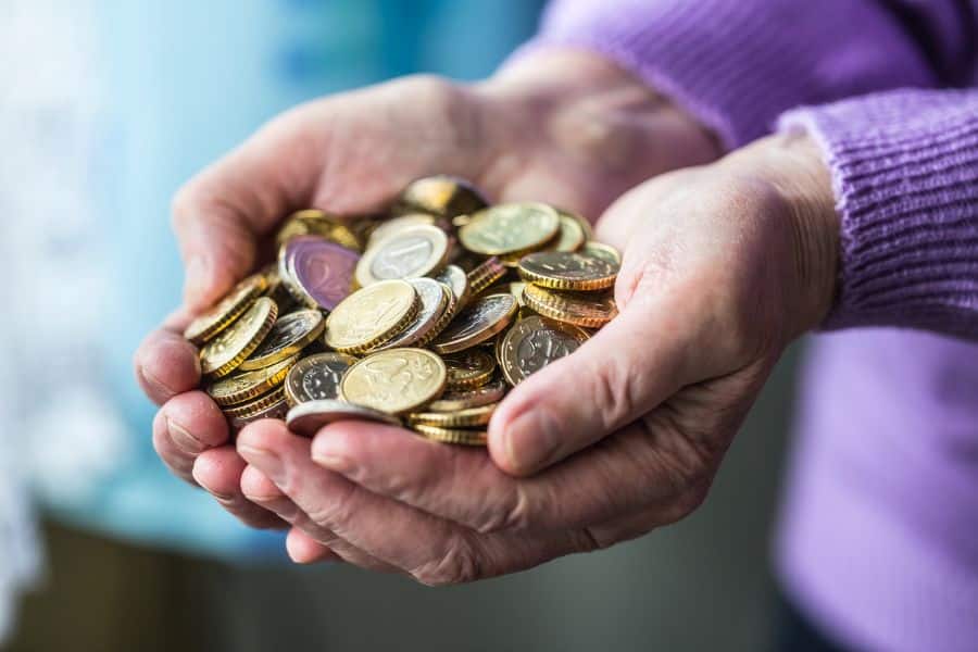 Close-up of elderly hands holding a pile of assorted coins, illustrating one of the simplest ways to save money by collecting spare change.