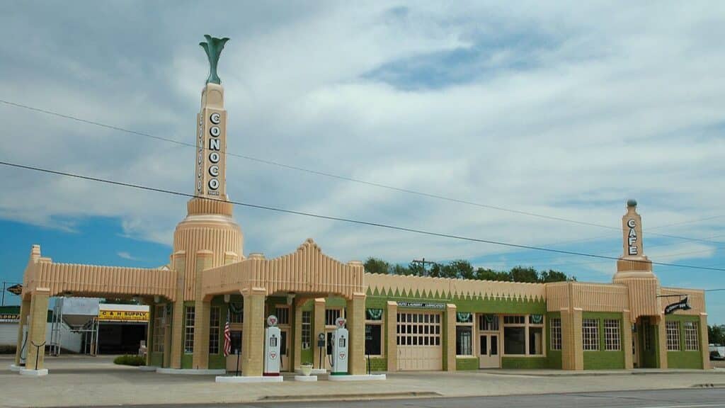 Art Deco-style building with tall towers marked “Conoco” and “Cafe,” featuring restored vintage gas pumps out front. A historic and architecturally iconic location on the map of restaurants on Route 66.