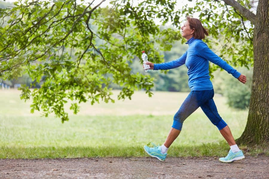 Woman speed walking on a trail while holding a water bottle, dressed in bright blue activewear. Brisk walking as an accessible everyday exercise for staying fit.