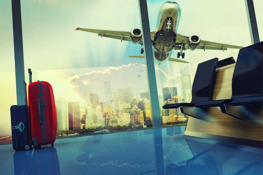 View from an airport terminal with two suitcases in the foreground and a plane flying past the window, illustrating smart travel hacks for efficient flying.