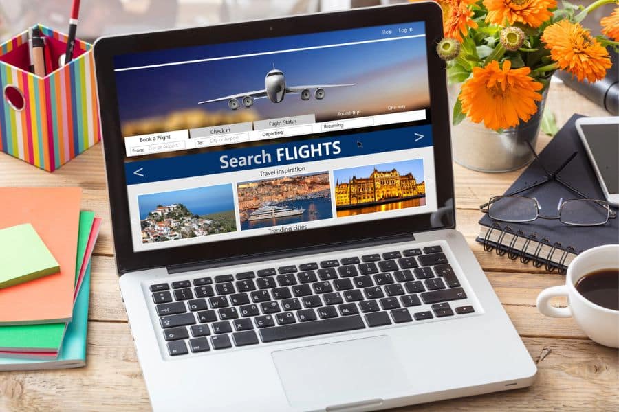 A laptop on a wooden desk displays a flight search website, emphasizing travel hacks for finding cheap flights.