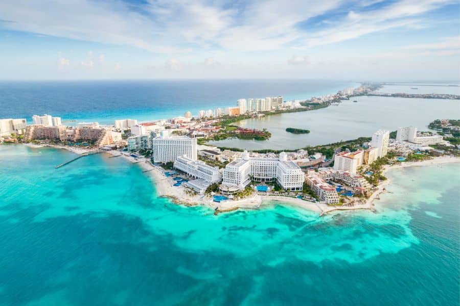 Aerial view of Cancun’s Hotel Zone with sprawling white resorts lining turquoise Caribbean waters and a lagoon on the opposite side. One of the most iconic all-inclusive resort getaways in Mexico.