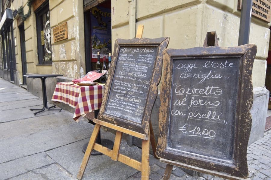 Rustic Italian restaurant with chalkboard menus outside displaying daily specials, offering local dining travel hacks for eating well on a budget.